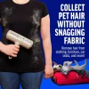 lint-remover-tool-on-black-clothing A person holding the roller against a black t-shirt covered in shed fur to show it cleans without snagging fabric. A small dog rests in a red suitcase in the corner
